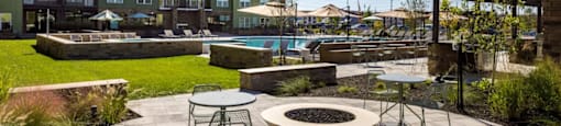 A patio with a fire pit and chairs is surrounded by a grassy area and a building in the background at Boardwalk at Research Park apartments in Huntsville, AL.