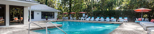 A pool surrounded by trees and chairs.