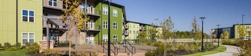 A green apartment complex with a clear blue sky in the background at Boardwalk at Research Park apartments in Huntsville, AL.
