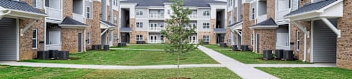 a tree in the middle of a grassy area in front of an apartment building