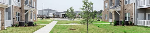 a grassy area with trees in front of an apartment complex