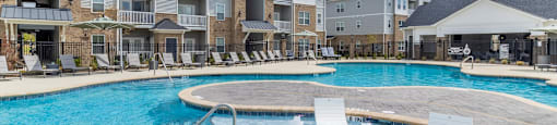 a large swimming pool with white lounge chairs in front of an apartment building