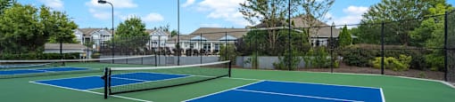 two tennis courts with houses in the background on a sunny day
