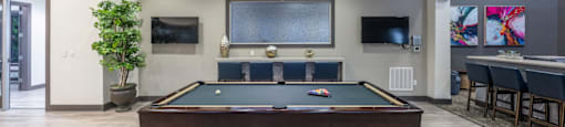 a pool table in the lobby of a clubhouse with a bar and a television