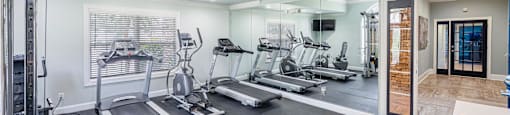 a gym with cardio machines and a ceiling fan