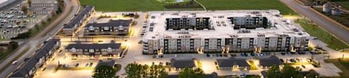 A sunset view of a large apartment complex with a green field in the foreground at Liam at Hays Farm in Huntsville, Alabama