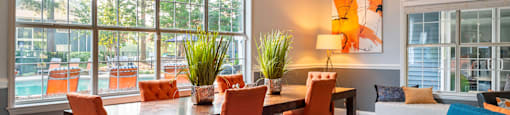 a living room with a large window and a wooden table with orange chairs