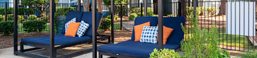 two blue couches with orange pillows sit on a sidewalk in front of a fence and