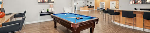 A room with a pool table and a bar area.