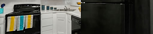 A black refrigerator stands in a kitchen with white cabinets.