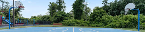 A blue basketball court with two hoops and a green grassy area in the foreground.