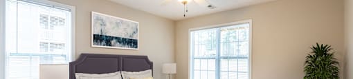 A bedroom with a large bed, a ceiling fan, and a potted plant.