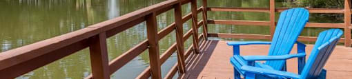 Two blue chairs on a wooden deck overlooking a pond.