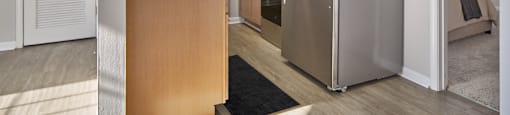 A modern kitchen with a refrigerator, wooden cabinets, and a black rug.