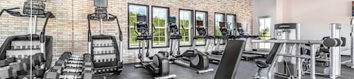 a gym with cardio equipment and weights on a brick wall