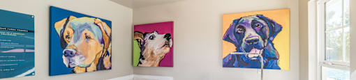 A room with a white desk and two paintings of dogs.