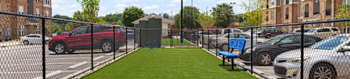 a green lawn in a fenced in area with cars in a parking lot