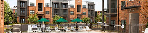 A swimming pool surrounded by chairs and tables in front of apartment buildings.