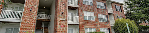 A red brick apartment building with a white railing and a white door.