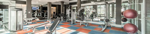 a gym with a colorful floor with exercise machines and a red ball
