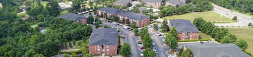 A large red brick building surrounded by trees and a parking lot.