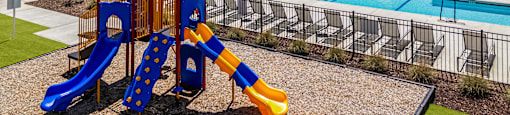 A playground with a blue and yellow slide in front of a building.