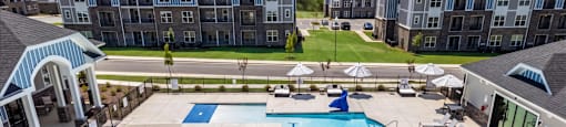 A large swimming pool surrounded by lounge chairs and apartment buildings in the background.