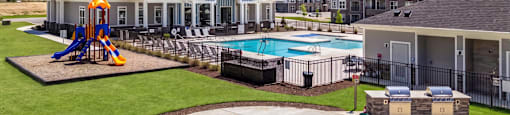 A playground area with a slide and swings is surrounded by a grassy area and a pool.