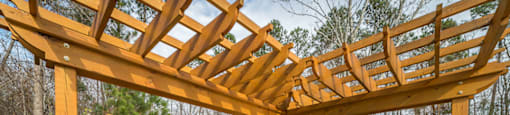 A wooden pergola with stone pillars and a black metal fence in the background.