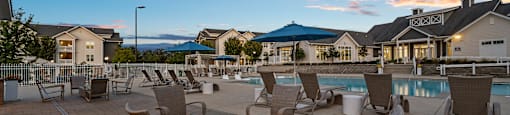 a swimming pool with chairs and tables at dusk