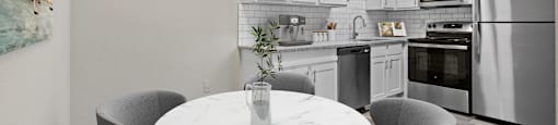 a kitchen with white cabinets and stainless steel appliances and a white marble table with four chairs