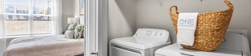 A small laundry room with a washer and dryer, a basket with a label on it, and a shelf with towels.