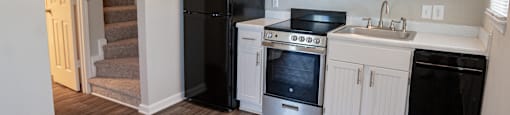 Spacious kitchen with white cabinetry,  black energy efficient appliances and plank style flooring