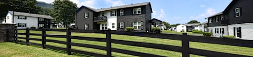 a black fence in front of a green field with houses in the background