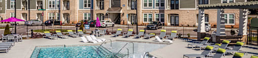 a swimming pool with lounge chairs in front of an apartment building
