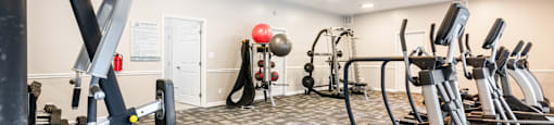 A gym with a variety of equipment including treadmills, weights, and a bench.