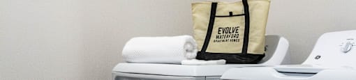 A white washing machine with a bag on top of it. at Evolve Waterford Apartments in Belville, NC