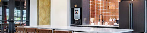 A clubhouse kitchen with a long island and chairs  at Evolve Waterford Apartments in Belville, NC