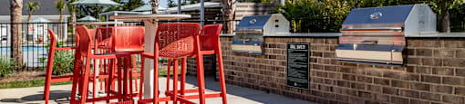 A set of red chairs are placed on a concrete  patio next to outdoor grills at Evolve Waterford Apartments in Belville, NC
