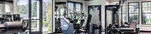 A gym with a variety of equipment including a bench press, a leg press, and a squat rack. at Evolve Waterford Apartments in Belville, NC