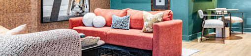 A seating area with a red couch and a grey chair at Evolve Waterford Apartments in Belville, NC