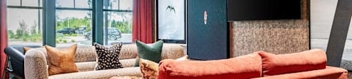 A  clubhouse with a red couch and a grey armchair at Evolve Waterford Apartments in Belville, NC.