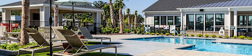 A pool area with a sun lounger and umbrella at Evolve Waterford Apartments in Belville, NC