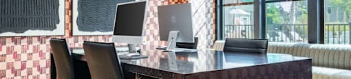 A black desk with two computers and two chairs in front of a window with a view of a green lawn at Evolve Waterford Apartments in Belville, NC.
