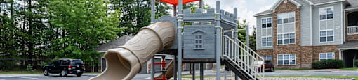 A playground with a red umbrella and a slide.