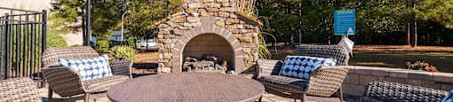 A patio with a stone fireplace and wicker chairs.