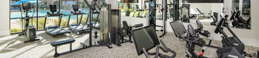 A gym with a variety of exercise equipment including treadmills, stationary bikes, and weight machines at Liam at Hays Farm in Huntsville, Alabama