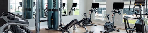 a fitness room with weights and cardio equipment and windows