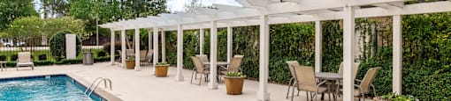 A pool with a white pergola and chairs around it.