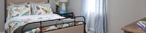 A bed with a metal frame and a floral comforter sits in a room with a carpeted floor and a window at 1287 Shoals apartments in Athens, GA.